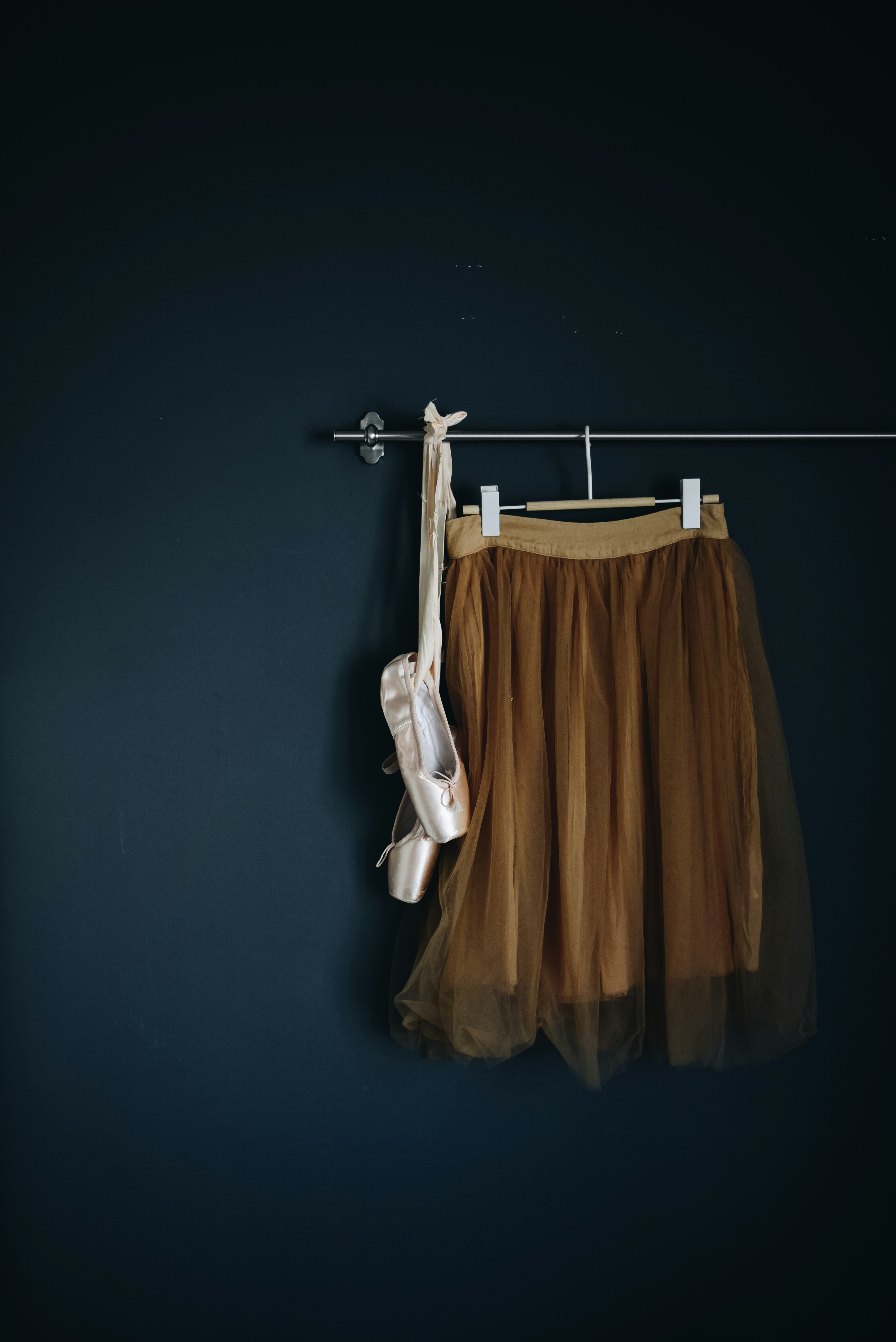 Solo dancer’s ballet skirt in a gold tulle on hanger  and pair of ballet shoes hanging on barre 