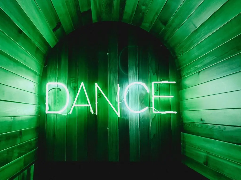 Image of a neon lights at the end of a hallway that says dance